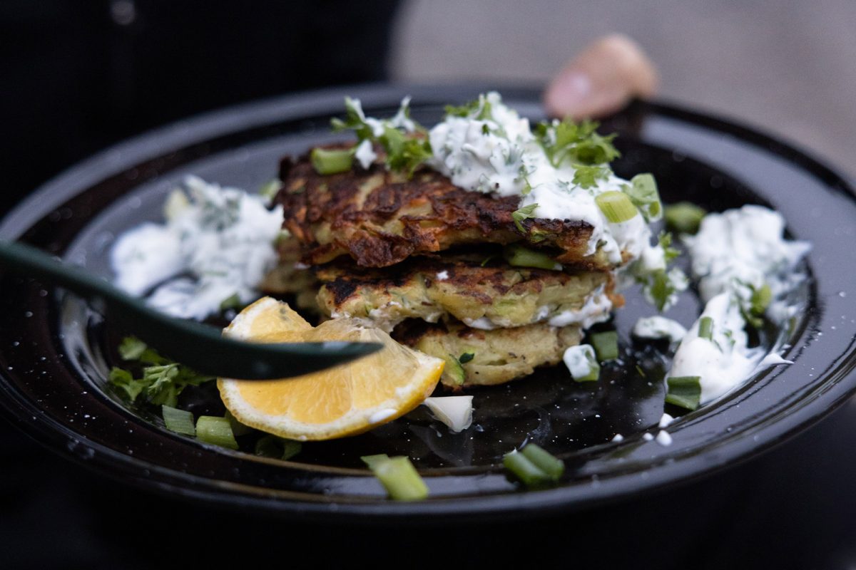 Zucchni and potato fritters on a black plate with zingy yogurt sauce and a wedge of lemon. 