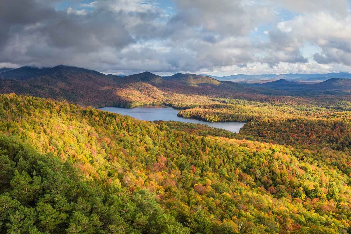 A view of Saranac Lake from above with hillsides of trees and fall foliage 