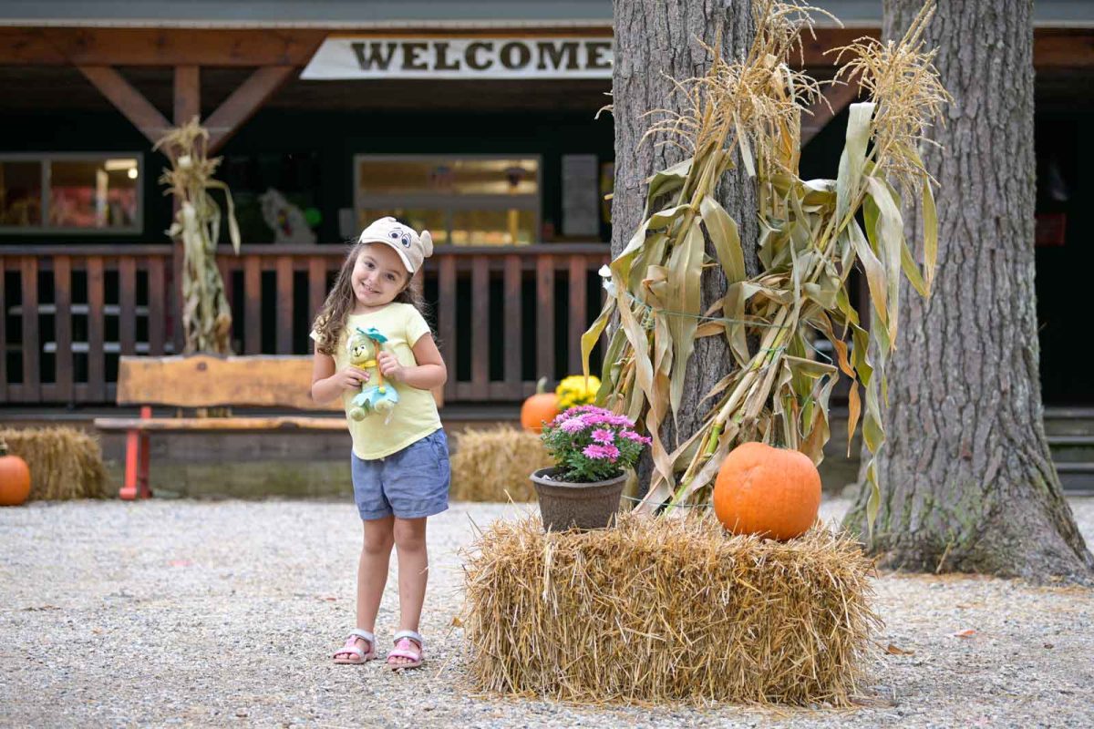 young girl next to pumpkins and corn stalk on Halloween camping site