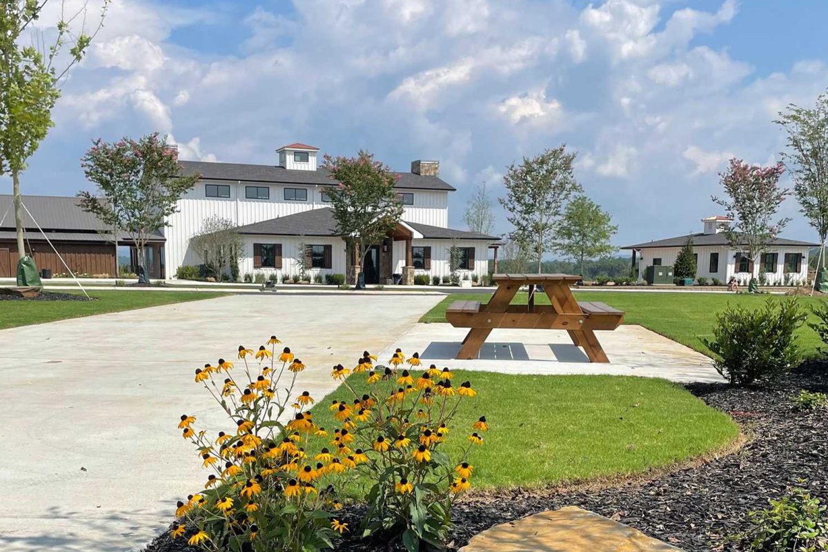 A white building with a picnic table in front of it with black-eyed Susans nearby. 