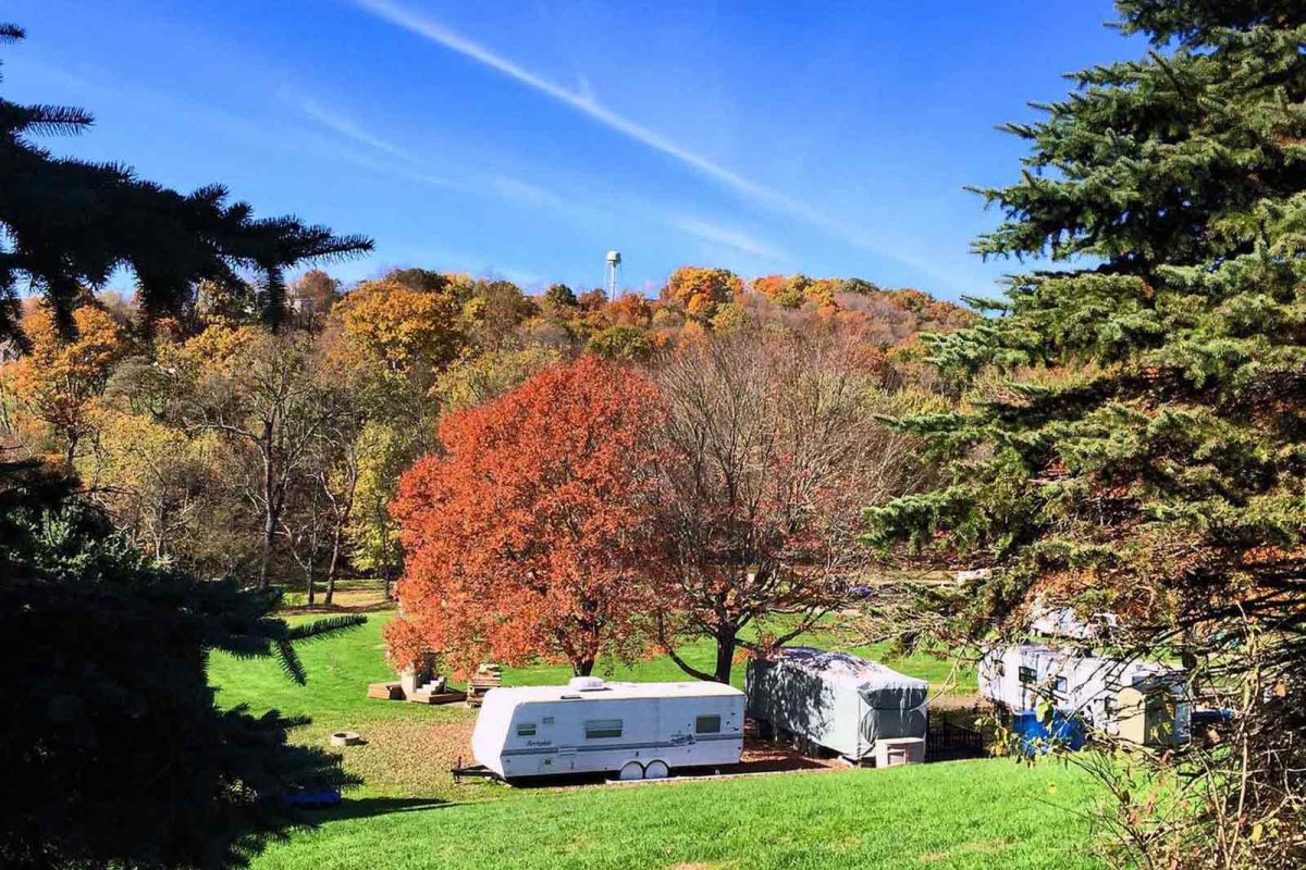 A bright red tree over an RV parked at an RV site with fall foliage in the background 