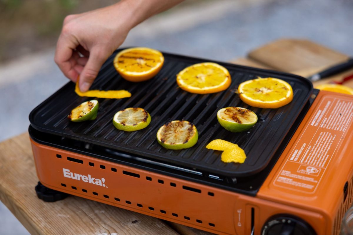 A hand places slices of citrus on a camping stove. 