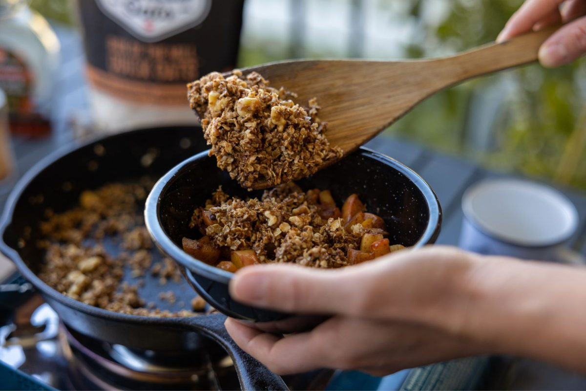 A spoonful of crisp for maple apple crisp scooped out of a caster iron skillet on a camp stove 