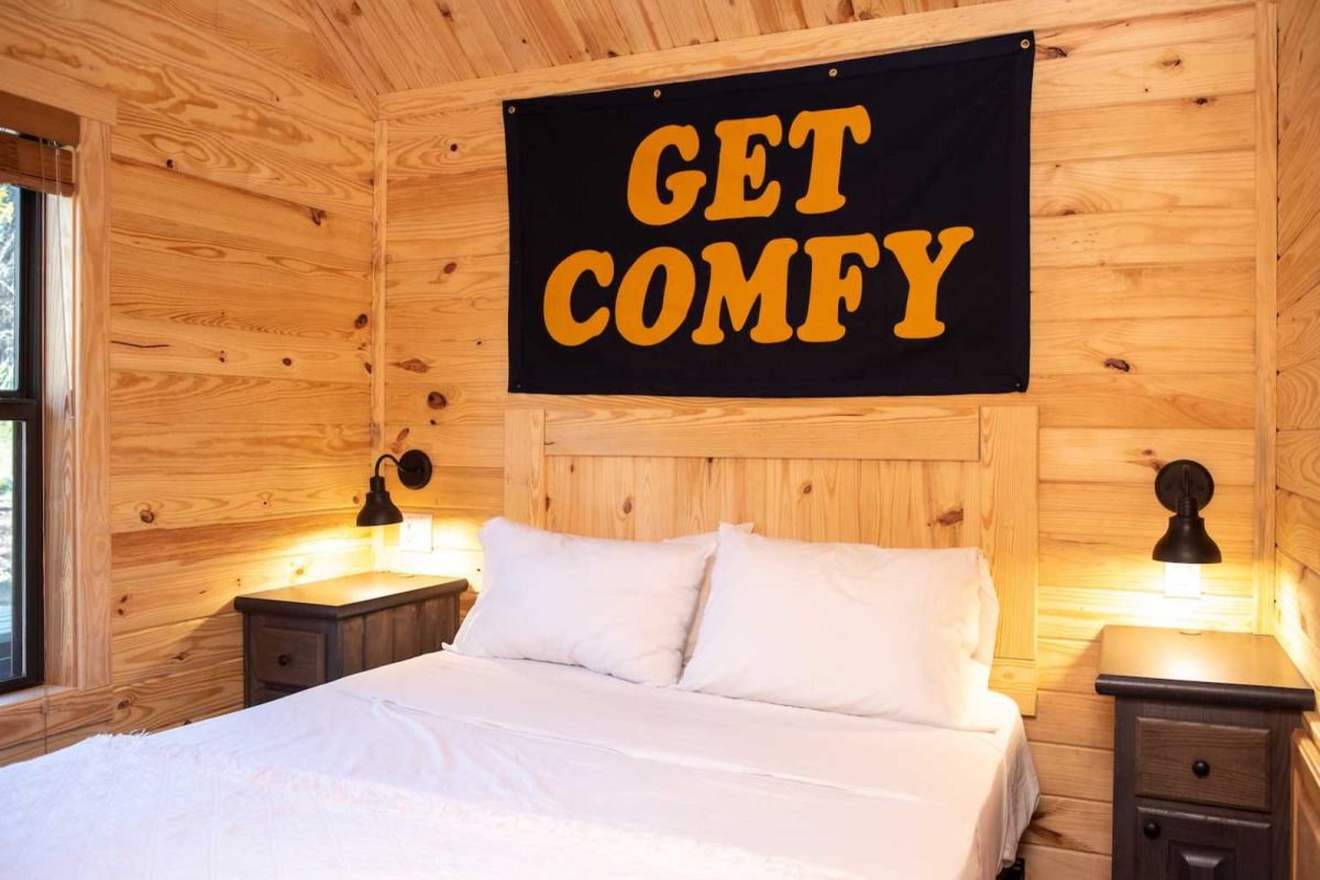 A bedroom in a cabin at Camp Fimfo with the sign "Get Comfy" above the bed 