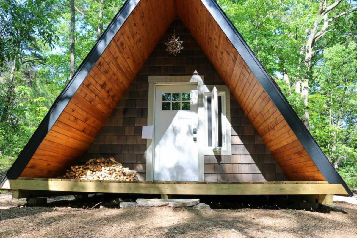 An a-frame cabin's front door with firewood on the porch at Detach Primitive, a campground with cabins 