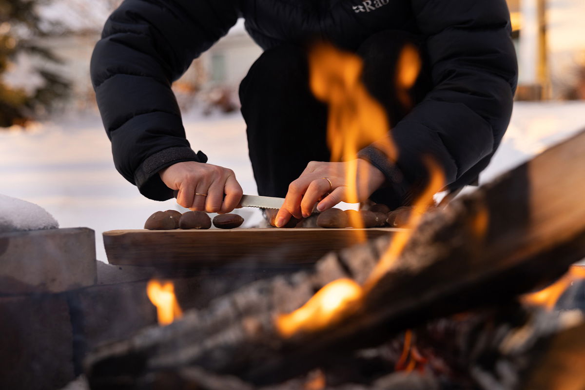 person cutting Xs on chestnuts by an open fire