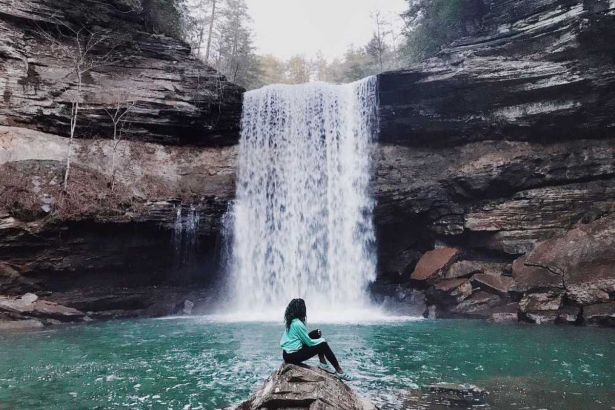 camper sitting on rock next to waterfall