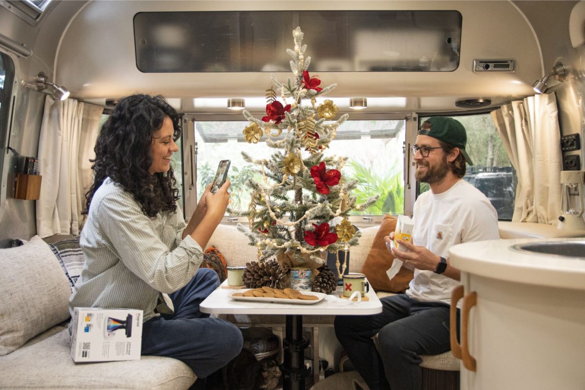 couple sharing gifts and taking photos by Christmas tree in their RV