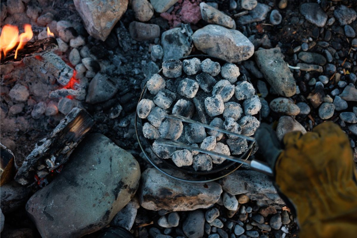 person layers coals onto dutch oven