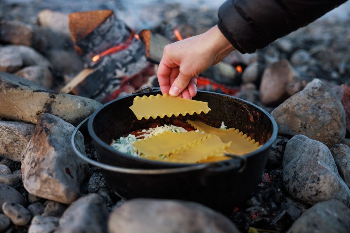 camper adding layers of pasta noodles to dutch oven lasagna recipe