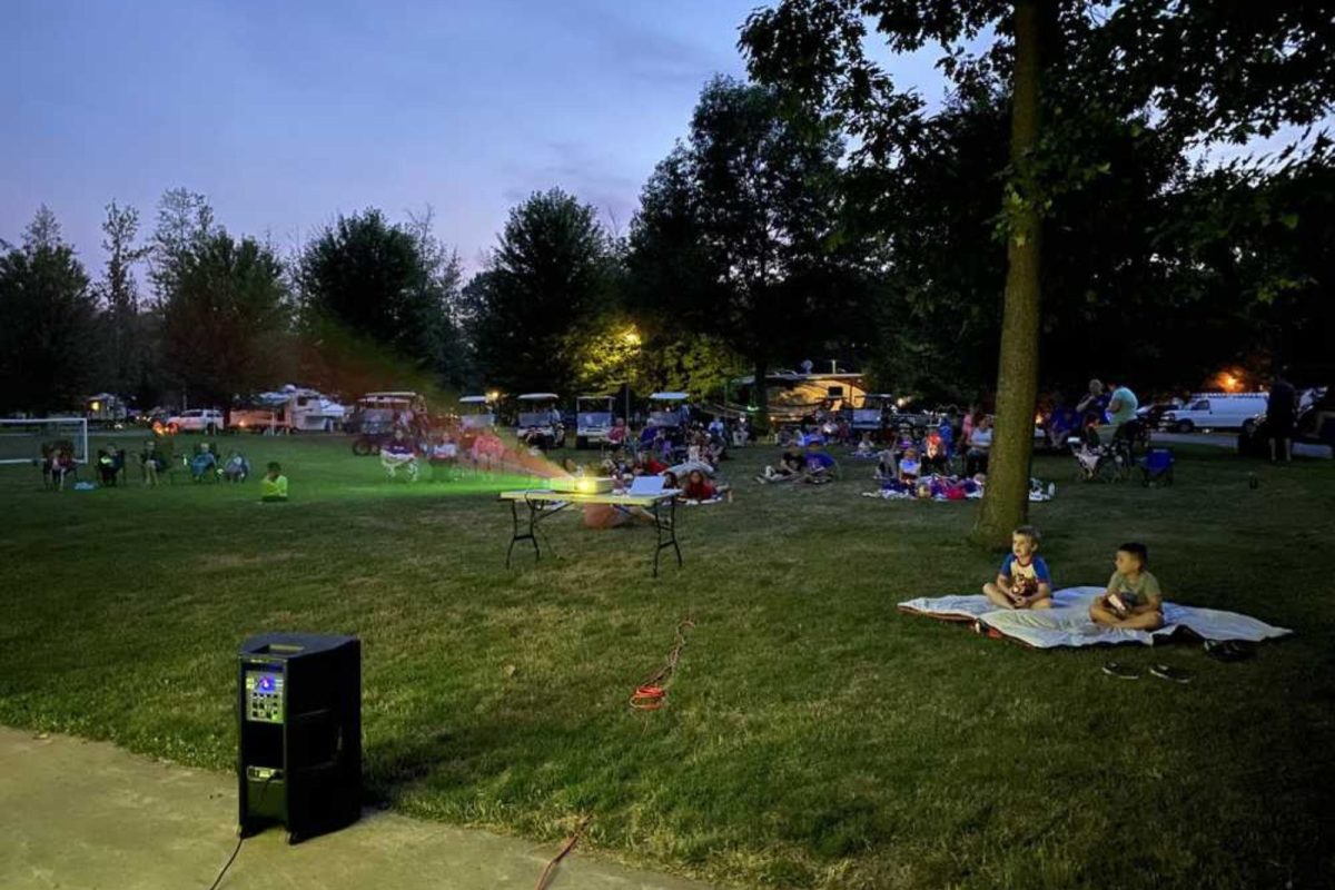 kids and families at campground near Buffalo, NY sitting on blankets at dusk watching a movie on the projector