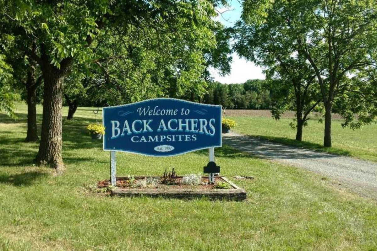 "Welcome to Back Archers Campsites" sign on grassy field with trees