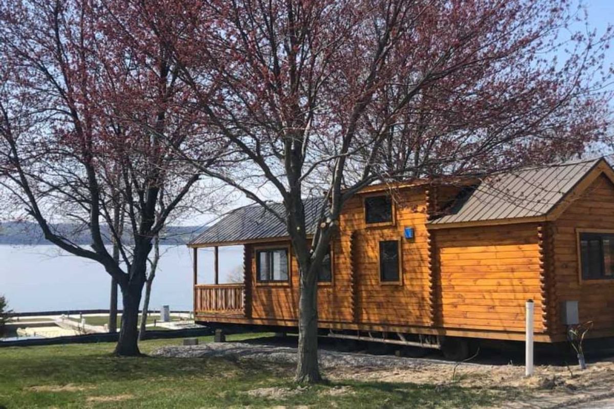 wood cabin next to lake and two trees with purple leaves at campground near Rochester, NY