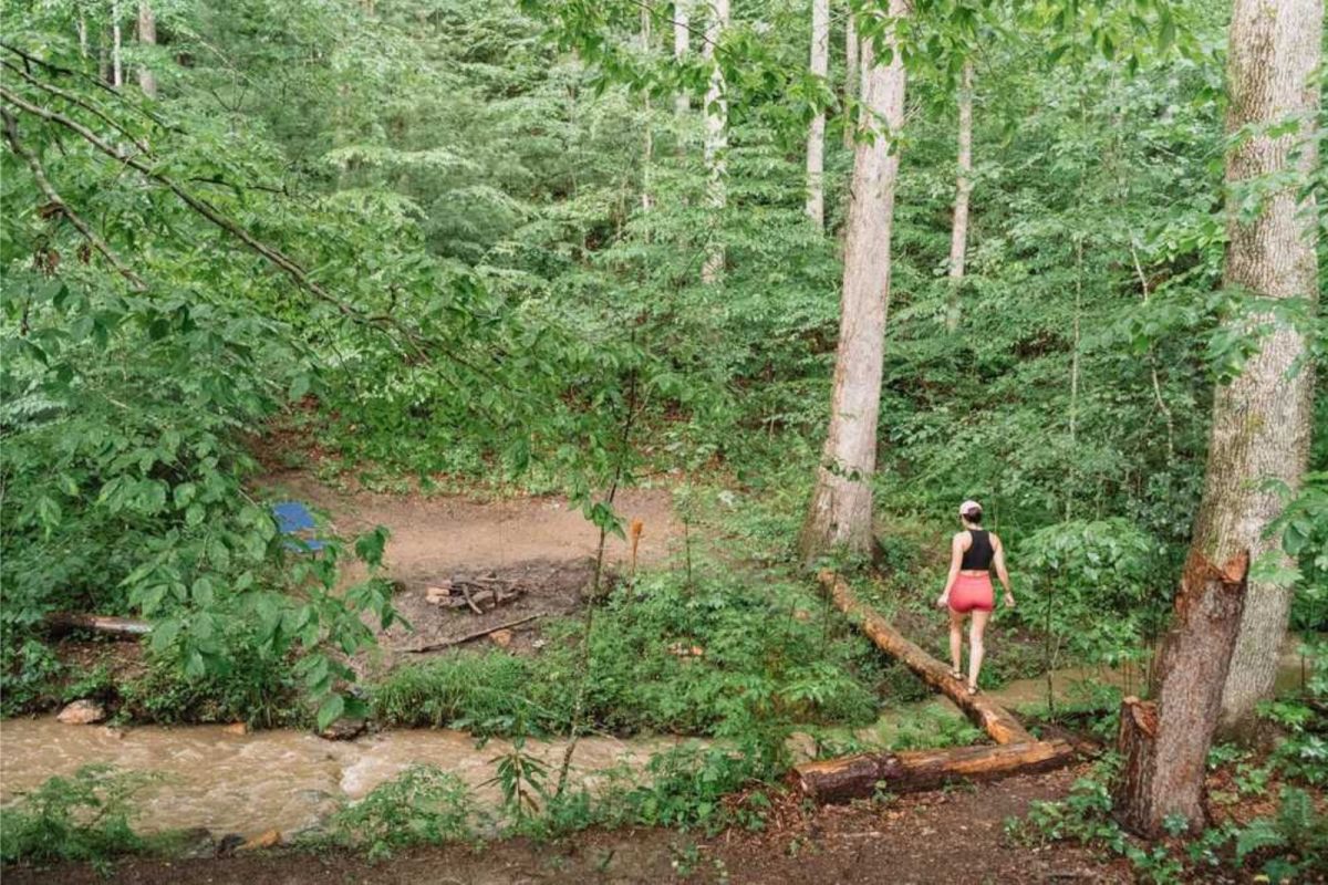 woman walking across log in woods at campground near Asheville