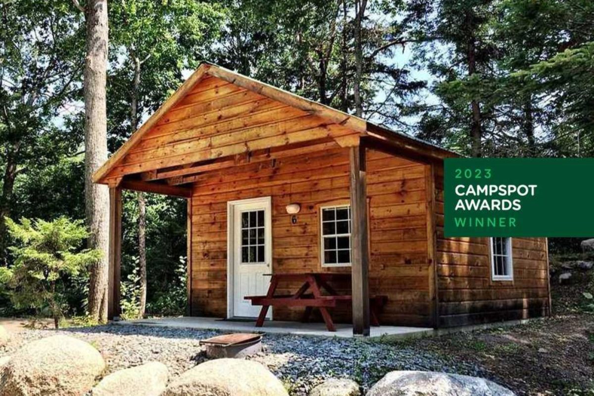 A cabin with a front porch and picnic table surrounded by trees. 