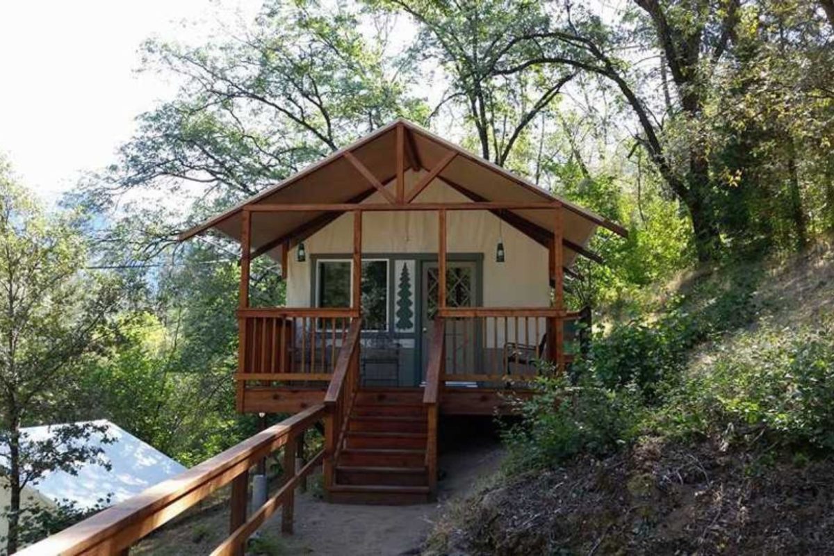 A cabin in the woods with a steps leading up to a front porch. 