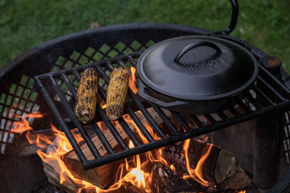 Corn and a cast iron skillet rest over open flames on a grill plate 