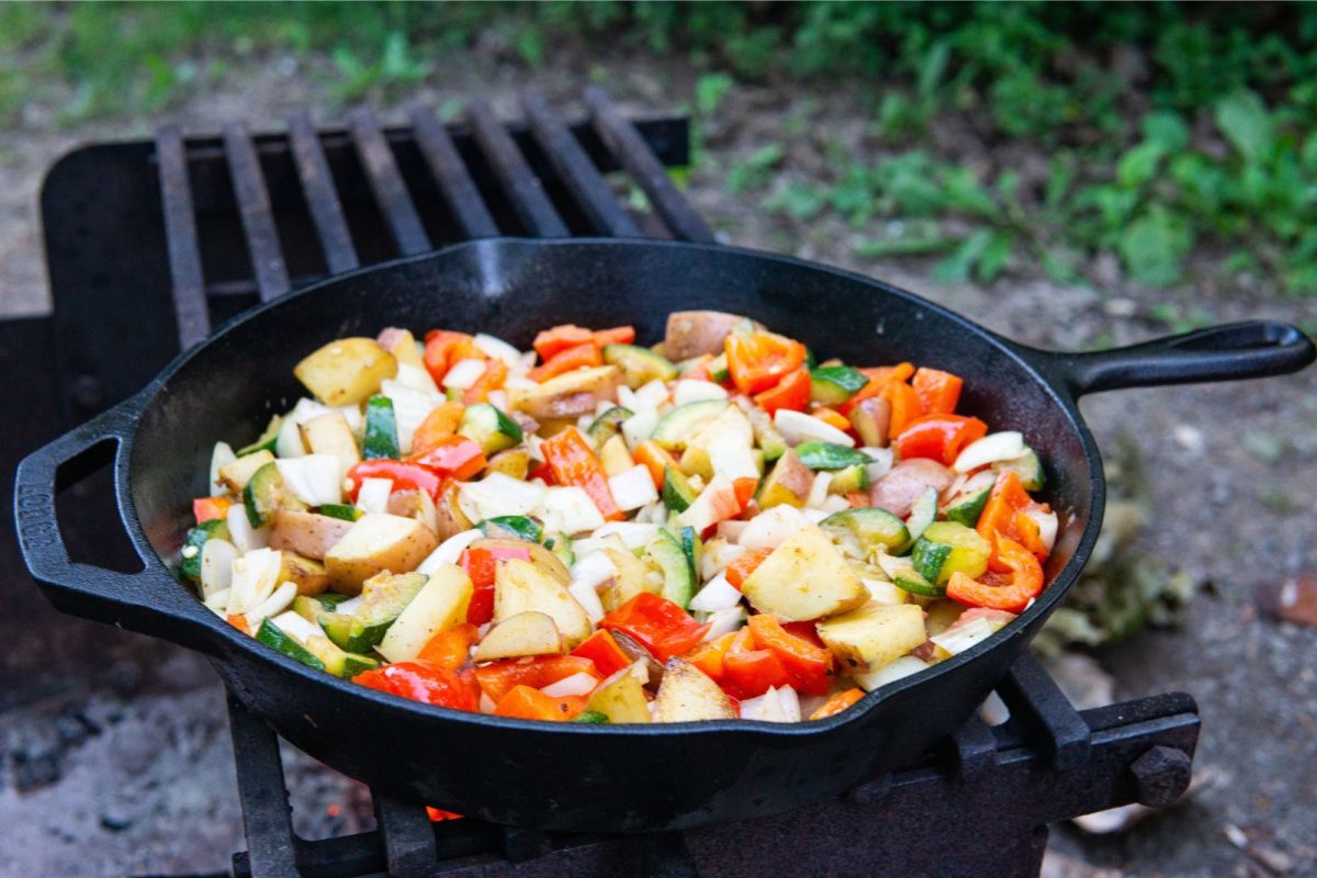 cast iron skillet over camping grill cooking vegetables