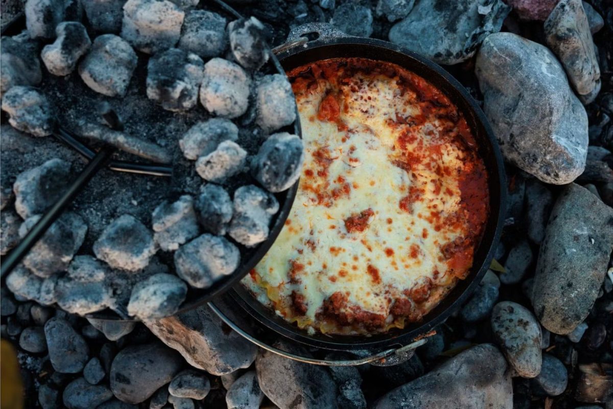 pulling off top of dutch oven that is filled with lasagna in camping grill