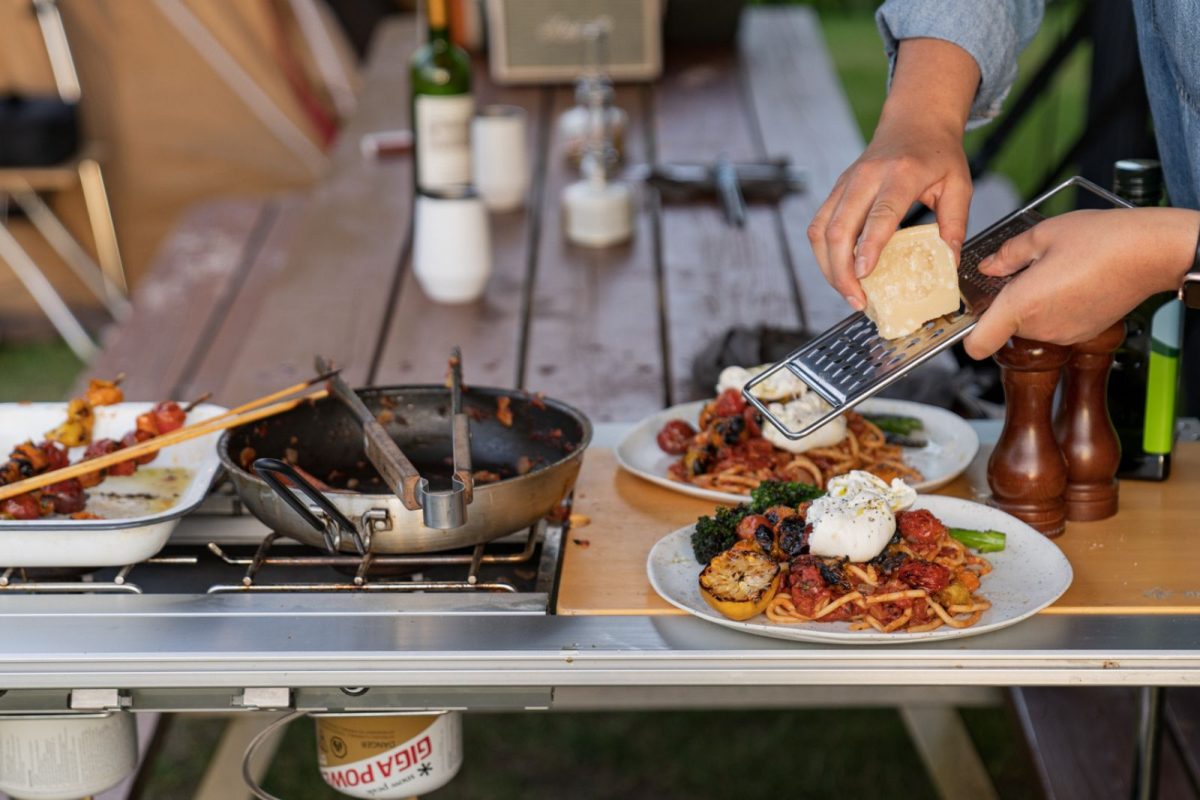 camper grating cheese over pasta next to camping grill