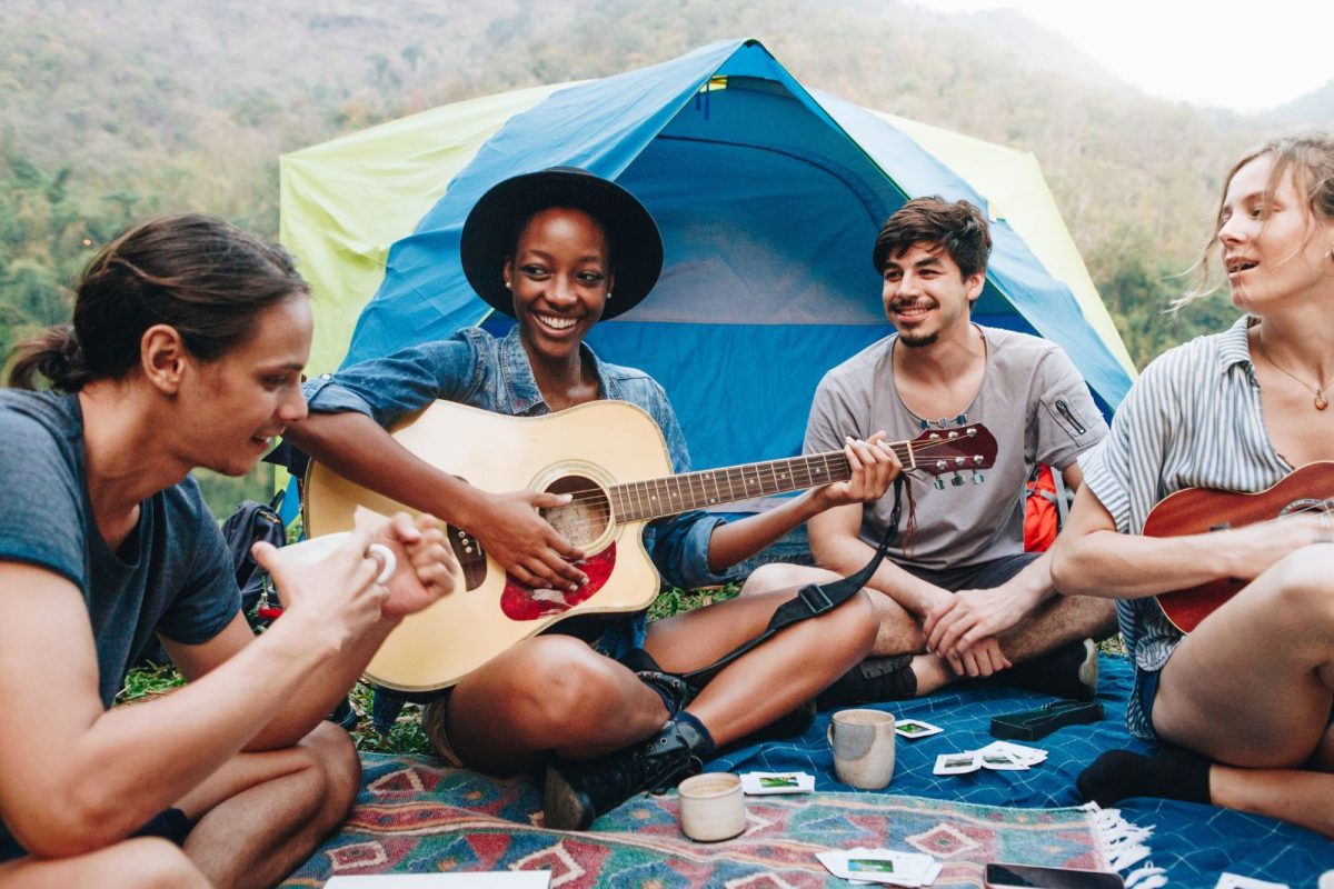 group of friends relax while camping with guitar and games outside tent