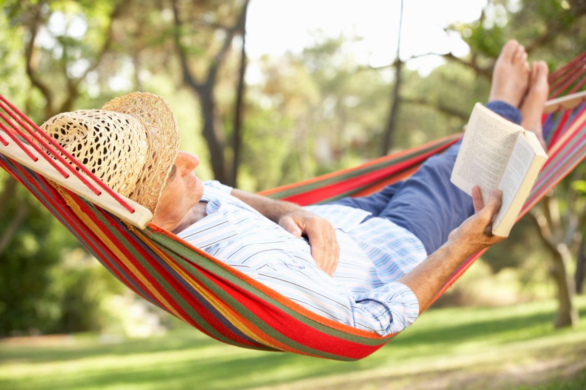 senior man relaxing while camping by reading book on hammock