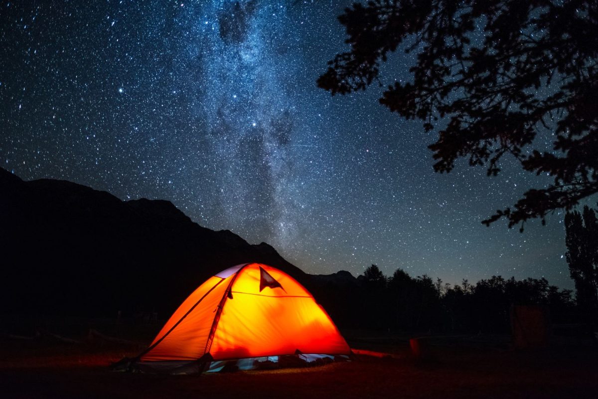 tent lit up during night with stars in background