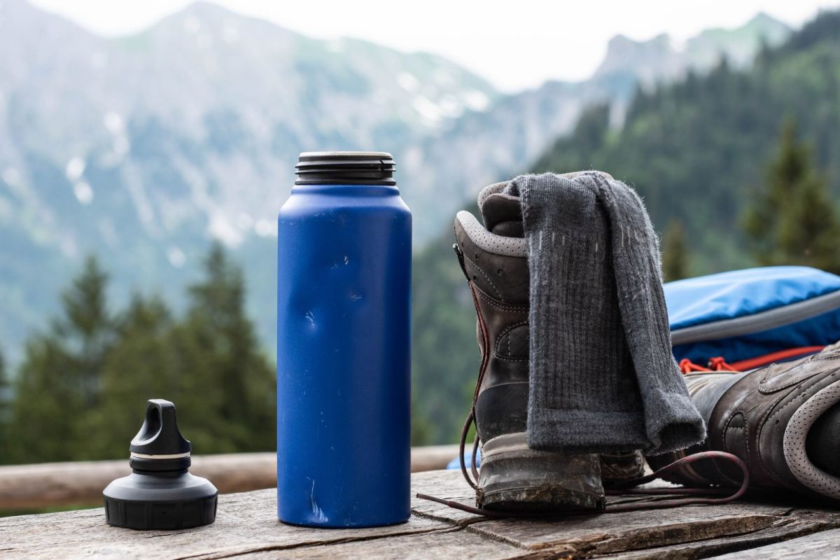 reusable water bottle next to hiking shoes with mountains in background