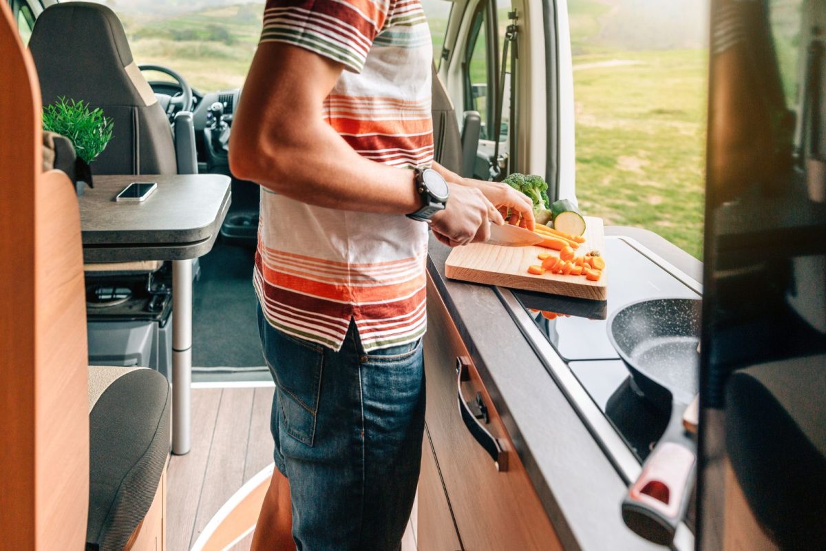 unrecognizable young man chopping veggies in RV to host gathering