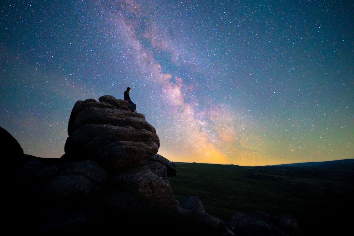 person sitting atop rock with Milky Way above during stargazing camping events