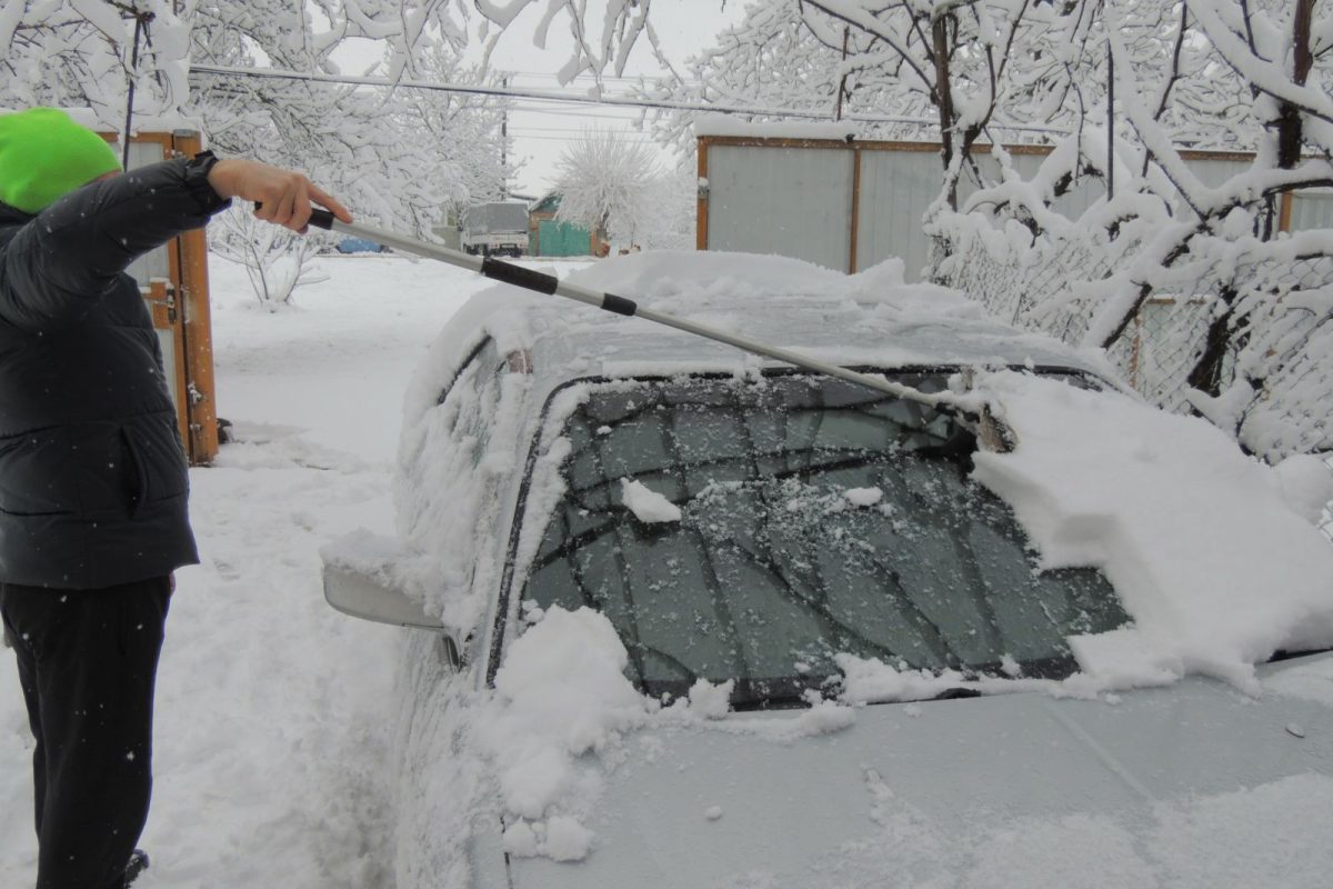 person scraping ice off of car during winter camping